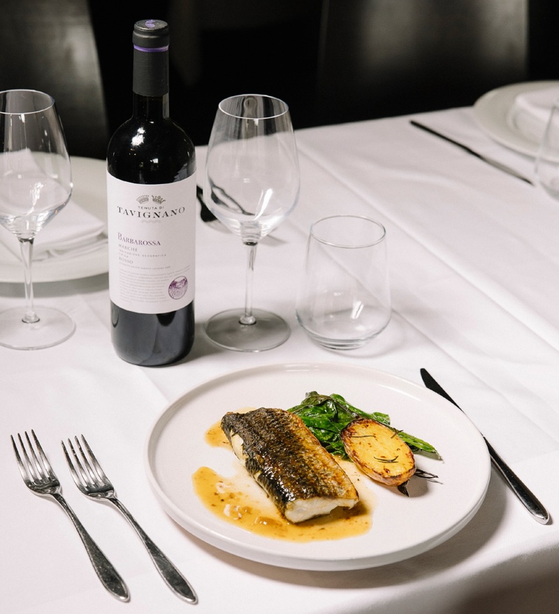 Filetto di branzino con patata arrosto e verdure, bottiglia di Barbarossa Tenuta di Tavignano su tovaglia bianca